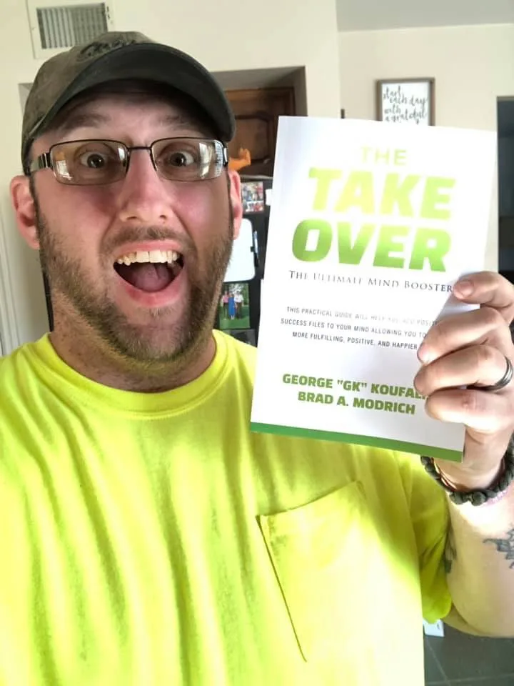 A reader holding a copy of The Takeover — the green title reading clearly at phone-camera distance.